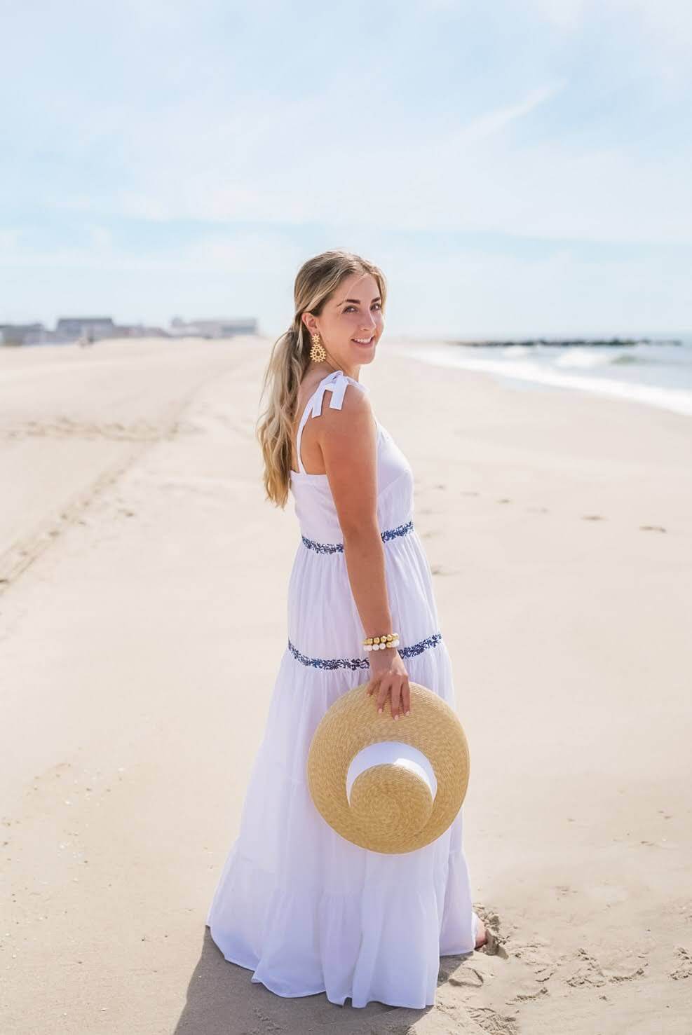 woman on beach in white sundress holding lisi lerch straw hat